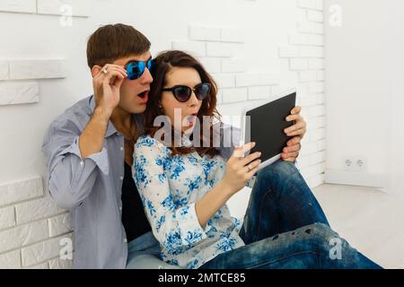 Couple heureux avec tablette, shopping en ligne, faire des commandes sur Internet assis à la maison dans le salon vide Banque D'Images