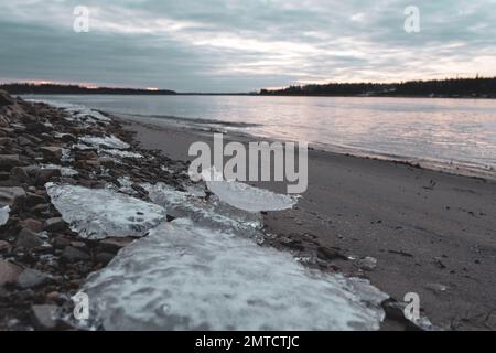De petits morceaux de glace se trouvent sur la rive sablonneuse de la rivière au début de l'hiver. Banque D'Images