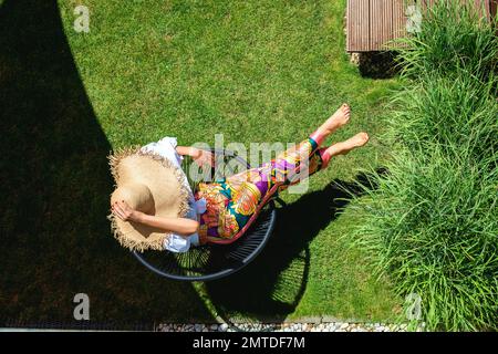 Photo en grand angle d'une femme reconnaissable portant un chapeau de paille et des vêtements de plage tout en se détendant à l'extérieur. Banque D'Images