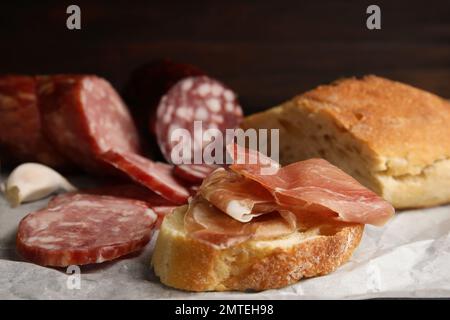 Délicieux pain avec prosciutto et autres saucisses sur papier parchemin, gros plan Banque D'Images