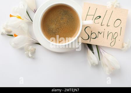 Carte avec mots HELLO SPRING, tasse de café et fleurs fraîches sur fond blanc, plat Banque D'Images