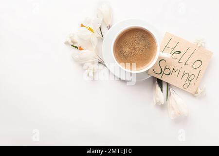 Carte avec mots HELLO SPRING, tasse de café et fleurs fraîches sur fond blanc, plat. Espace pour le texte Banque D'Images