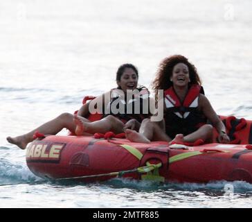 Rihanna ne peut pas arrêter de rire car elle aime une promenade sur « Big Mable » avec trois pals, qui une par une se détache sur le lit flottant et se jette dans l'océan. Attaché à un hors-bord, Big Mable a fait cracher les filles le long de l'eau au coucher du soleil. Après la promenade, Rihanna a dû réorganiser son bikini, la Barbade, 4 août 2011. Banque D'Images