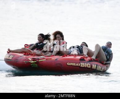 Rihanna ne peut pas arrêter de rire car elle aime une promenade sur « Big Mable » avec trois pals, qui une par une se détache sur le lit flottant et se jette dans l'océan. Attaché à un hors-bord, Big Mable a fait cracher les filles le long de l'eau au coucher du soleil. Après la promenade, Rihanna a dû réorganiser son bikini, la Barbade, 4 août 2011. Banque D'Images