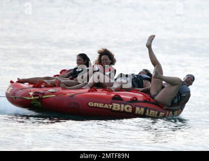 Rihanna ne peut pas arrêter de rire car elle aime une promenade sur « Big Mable » avec trois pals, qui une par une se détache sur le lit flottant et se jette dans l'océan. Attaché à un hors-bord, Big Mable a fait cracher les filles le long de l'eau au coucher du soleil. Après la promenade, Rihanna a dû réorganiser son bikini, la Barbade, 4 août 2011. Banque D'Images