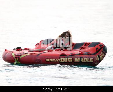 Rihanna ne peut pas arrêter de rire car elle aime une promenade sur « Big Mable » avec trois pals, qui une par une se détache sur le lit flottant et se jette dans l'océan. Attaché à un hors-bord, Big Mable a fait cracher les filles le long de l'eau au coucher du soleil. Après la promenade, Rihanna a dû réorganiser son bikini, la Barbade, 4 août 2011. Banque D'Images