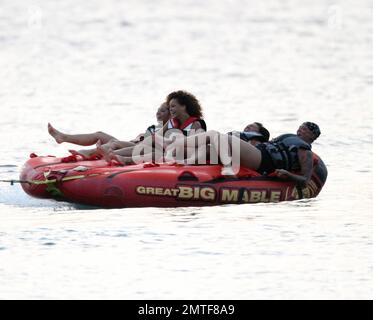 Rihanna ne peut pas arrêter de rire car elle aime une promenade sur « Big Mable » avec trois pals, qui une par une se détache sur le lit flottant et se jette dans l'océan. Attaché à un hors-bord, Big Mable a fait cracher les filles le long de l'eau au coucher du soleil. Après la promenade, Rihanna a dû réorganiser son bikini, la Barbade, 4 août 2011. Banque D'Images