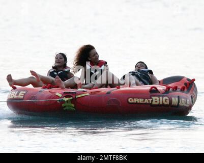 Rihanna ne peut pas arrêter de rire car elle aime une promenade sur « Big Mable » avec trois pals, qui une par une se détache sur le lit flottant et se jette dans l'océan. Attaché à un hors-bord, Big Mable a fait cracher les filles le long de l'eau au coucher du soleil. Après la promenade, Rihanna a dû réorganiser son bikini, la Barbade, 4 août 2011. Banque D'Images