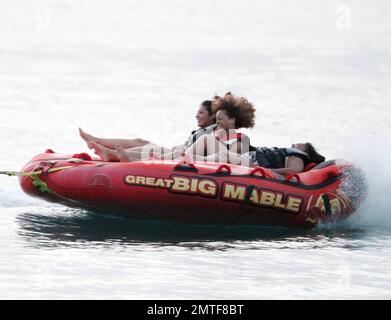 Rihanna ne peut pas arrêter de rire car elle aime une promenade sur « Big Mable » avec trois pals, qui une par une se détache sur le lit flottant et se jette dans l'océan. Attaché à un hors-bord, Big Mable a fait cracher les filles le long de l'eau au coucher du soleil. Après la promenade, Rihanna a dû réorganiser son bikini, la Barbade, 4 août 2011. Banque D'Images