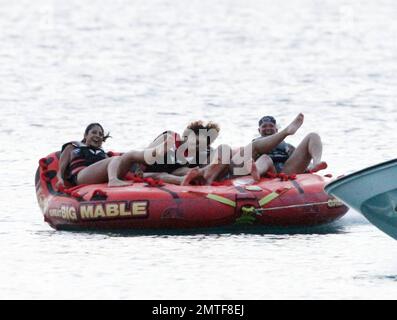 Rihanna ne peut pas arrêter de rire car elle aime une promenade sur « Big Mable » avec trois pals, qui une par une se détache sur le lit flottant et se jette dans l'océan. Attaché à un hors-bord, Big Mable a fait cracher les filles le long de l'eau au coucher du soleil. Après la promenade, Rihanna a dû réorganiser son bikini, la Barbade, 4 août 2011. Banque D'Images