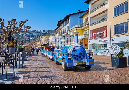 ASCONA, SUISSE - 28 MARS 2022 : le train touristique de style vintage fait le tour de la Piazza Giuseppe Motta, bordée de maisons historiques et d'un petit restaurant Banque D'Images