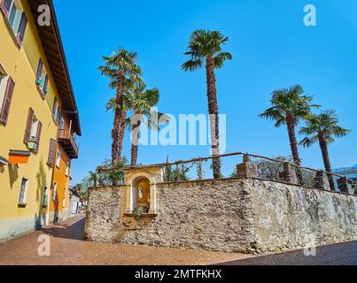 Le mur de pierre médiéval sur la via delle Cappelle avec de grands palmiers derrière elle et une petite chapelle construite dans le mur, Ascona, Suisse Banque D'Images