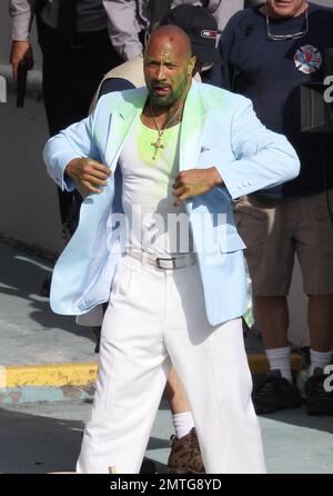 EXCLUSIF !! Portant une veste bleue pour bébé, une chemise blanche, un pantalon blanc, des chaussures blanches, un collier crucifix et ce qui semble être de la goo verte sur son visage et sa poitrine, Dwayne « The Rock » Johnson et son double stunt sont vus sur le terrain pour filmer une séquence d'action pour son prochain film « pain & gain ». Le film est réalisé par Michael Bay, réalisateur de 'Transformerss', et devrait sortir en 2013. Maimi, Floride. 14th avril 2012. Banque D'Images