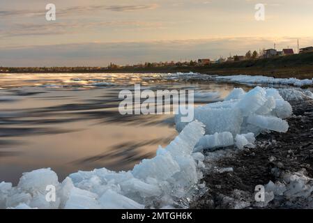 Les restes de la dernière glace de printemps sur la rivière Vilyui à Yakutia se trouvent sur la rive et flottent sur la toile de fond du village de suntar pendant le Banque D'Images