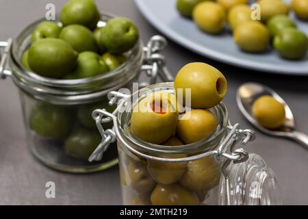Olives vertes dans des pots en verre. Olives sur une assiette bleue. Gros plan. Arrière-plan gris. Banque D'Images