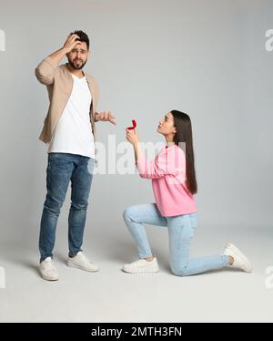 Jeune femme avec anneau d'engagement faisant la proposition de mariage à son petit ami sur fond gris clair Banque D'Images