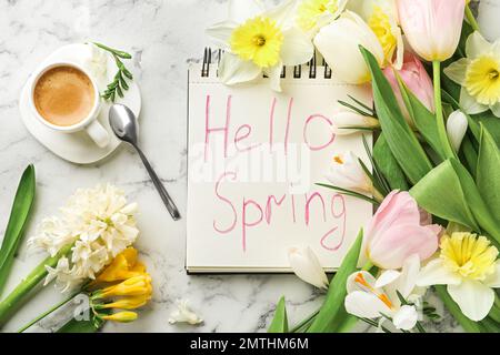 Carnet avec mots HELLO SPRING, tasse de café et fleurs fraîches sur table en marbre blanc, plat Banque D'Images