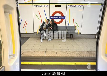 Londres, Angleterre, Royaume-Uni. Métro de Londres : couple assis sur un banc sur la plate-forme de la station Embankment. Banque D'Images