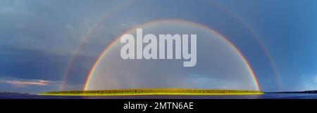 Panorama d'un double arc-en-ciel lumineux au-dessus de la rivière Vilyui après une pluie contre un ciel bleu avec des nuages et des arbres sur la rive à Yakutia. Banque D'Images