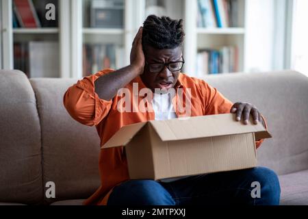 Un jeune homme afro-américain déçu ouvre la boîte à colis Banque D'Images