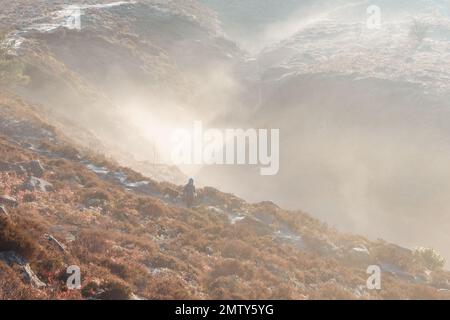 Une femme marchant sur un chemin le long d'un froid hiver sur Ilkley Moor avec un peu de brume de moody tourbillonnant créant l'atmosphère dans le fond et un lourd Banque D'Images