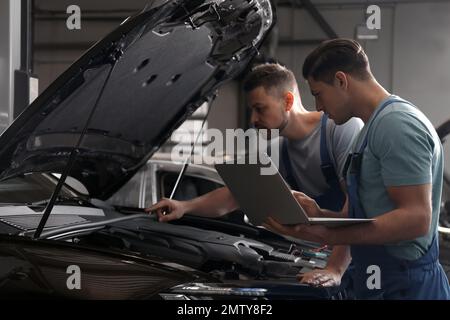 Mécanique avec ordinateur portable faisant le diagnostic de voiture à l'atelier de réparation automobile Banque D'Images