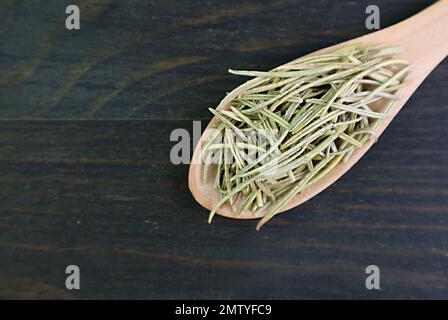 Vue de dessus du romarin séché aromatique dans une cuillère sur fond en bois noir Banque D'Images