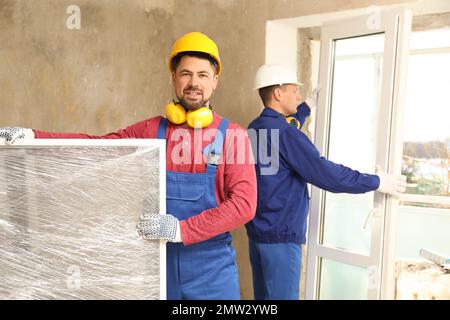 Ouvriers en uniforme installant des fenêtres en plastique à l'intérieur Banque D'Images