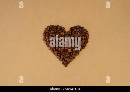 forme de coeur faite en grains de café rôtis sur un fond de papier artisanal, valentin de café, amateurs de café Banque D'Images