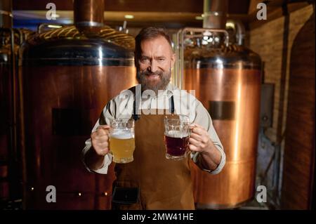 Brasseur senior satisfait posant pour caméra avec de la bière pâle et de la bière foncée pinte Banque D'Images