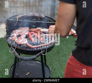 Un homme cuisant du bacon typiquement espagnol et un barbecue chorizo sur un grill à l'extérieur Banque D'Images