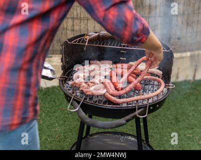 Un homme cuisant du bacon typiquement espagnol et un barbecue chorizo sur un grill à l'extérieur Banque D'Images