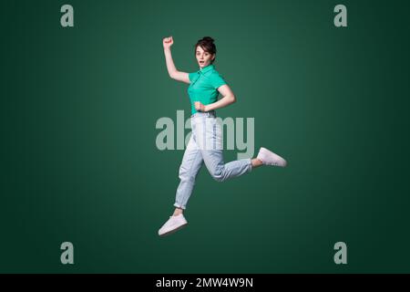 Profil complet photo de côté de la jeune femme sautant avec l'expression du visage choqué isolé sur fond vert Banque D'Images
