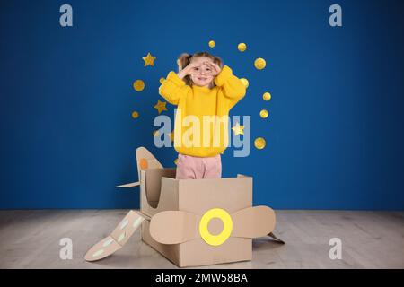 Mignon petit enfant jouant avec un avion en carton près du mur bleu Banque D'Images