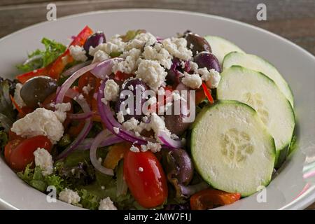 Salade grecque au concombre, tomates cerises, feta, oignons rouges, olives kalamata, et de la laitue croustillante, dans un bol blanc avec un éclairage latéral spectaculaire Banque D'Images