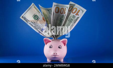 Banque de porc rose avec dollars à l'intérieur sur fond bleu avec espace de copie sur le côté Banque D'Images