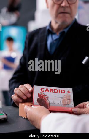 Vieil homme consultant sur les médicaments cardiaques au comptoir, demandant à la caissière de pharmacie au sujet des suppléments explication d'instruction. Assistant pharmaceutique tenant l'emballage de vitamines au moment de la vérification Banque D'Images