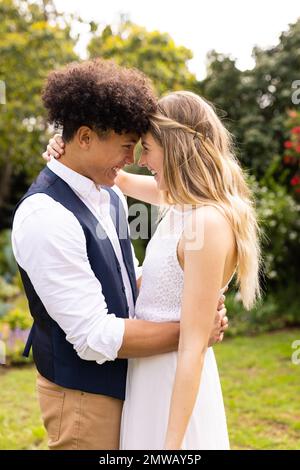 Vertical de la bonne diversité mariée et marié touchant les têtes, embrassant au mariage dans le jardin Banque D'Images