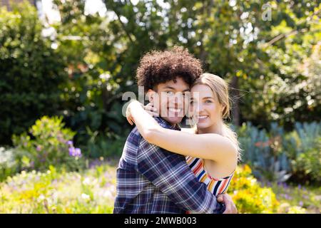 Portrait d'un couple heureux et diversifié, souriant et enveloppant dans un jardin ensoleillé Banque D'Images