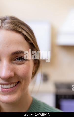 Portrait vertical à moitié de visage de femme blanche blonde souriante dans la cuisine à la maison, espace de copie Banque D'Images