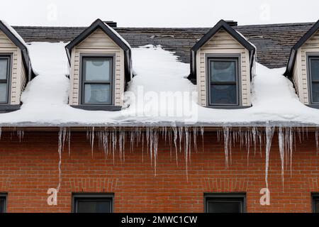 Maison résidentielle avec fenêtres sur le toit couverte de neige et de glaçons suspendus en hiver. Banque D'Images