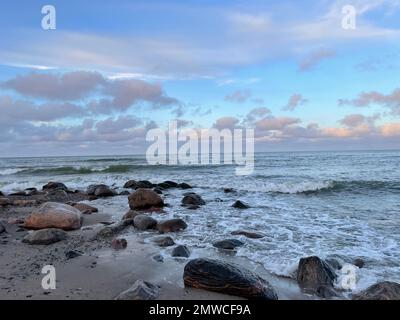 Une vue panoramique sur les vagues de la mer Baltique s'écrasant dans les rochers sur une plage de sable au coucher du soleil Banque D'Images