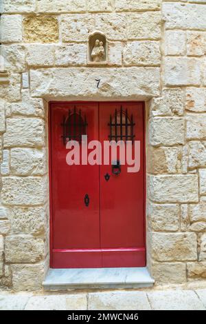 Vieux rouge peint avec des barres en fer forgé noir porte d'entrée en bois avec des grilles en fer forgé ornées sur la façade d'un immeuble résidentiel à Mdina, Malte. Banque D'Images