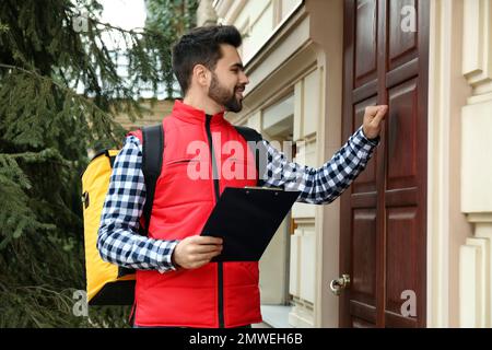 Messagerie avec sac thermo et presse-papiers frappant dans la maison du client. Service de livraison de nourriture Banque D'Images