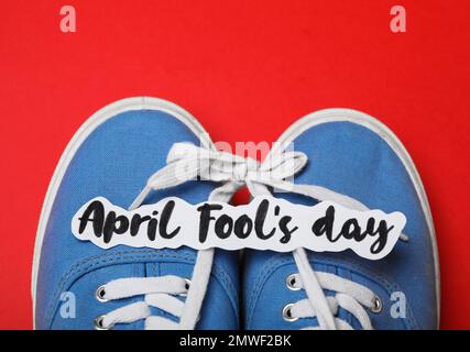 Chaussures attachées ensemble et note avec la phrase AVRIL IDIOT'S DAY sur fond rouge, vue de dessus Banque D'Images