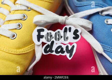 Chaussures attachées ensemble et note avec l'expression DE LA JOURNÉE DE L'IMBÉCILE sur fond rose, gros plan Banque D'Images