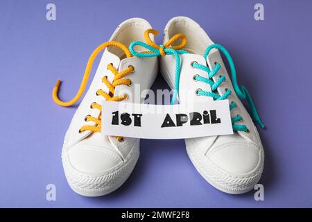 Chaussures attachées ensemble et note avec la phrase 1st AVRIL sur fond lilas. Journée des imbéciles Banque D'Images