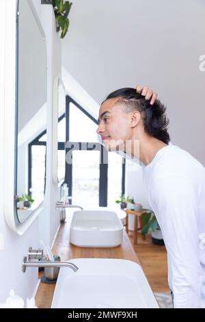 Joyeux biracial homme regardant dans le miroir dans la salle de bains Banque D'Images