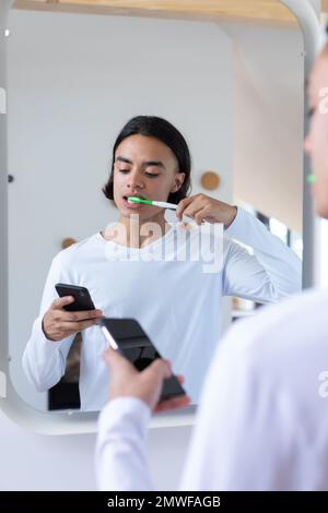 Heureux biracial homme se brossant les dents et en utilisant le smartphone dans la salle de bains Banque D'Images