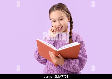 Petite fille mordant des ongles tout en lisant le livre sur fond lilas Banque D'Images